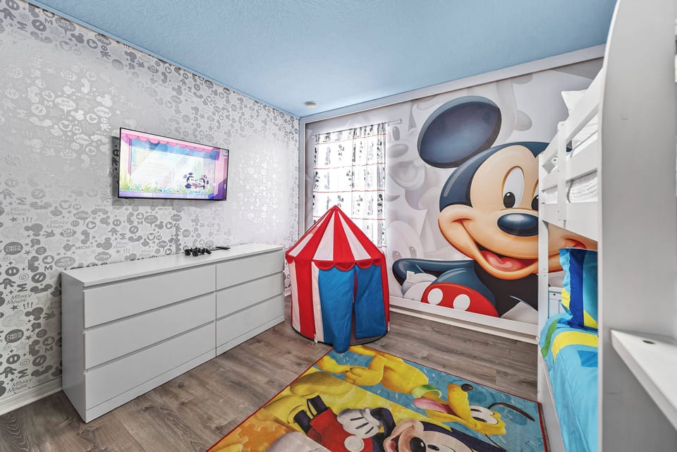This bright and playful children's room, adorned with charming Mickey Mouse decor, creates a fun atmosphere for your little ones. Cozy bunk beds ensure restful nights, while the vibrant carpet and tent add an adventurous touch.