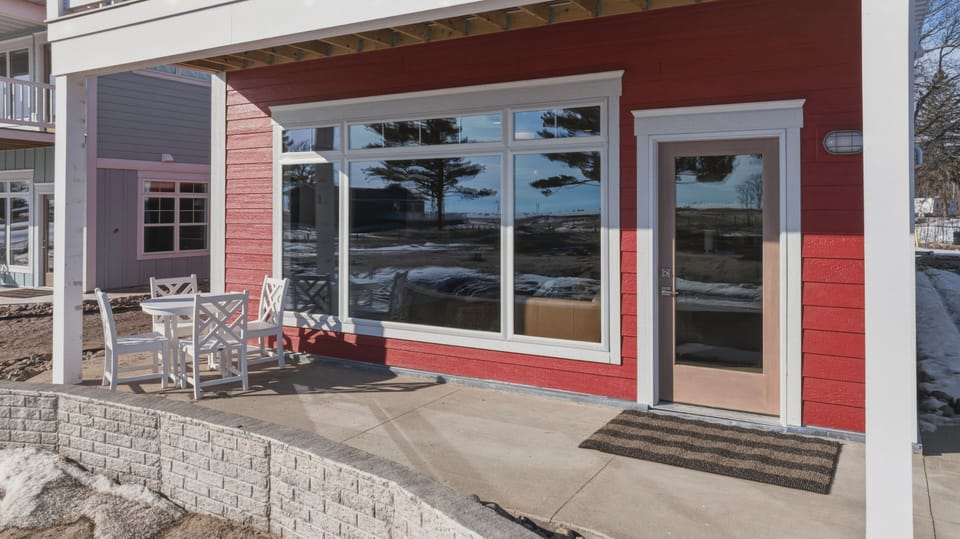 Ground level patio with bistro seating large windows and red siding