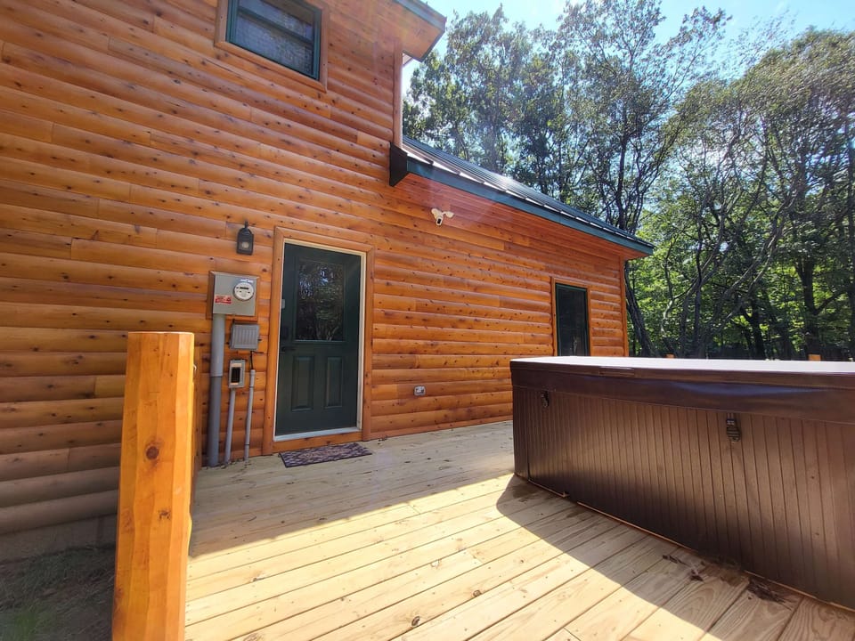Rear exterior of cabin showing elevated deck, hot tub area, and tree canopy