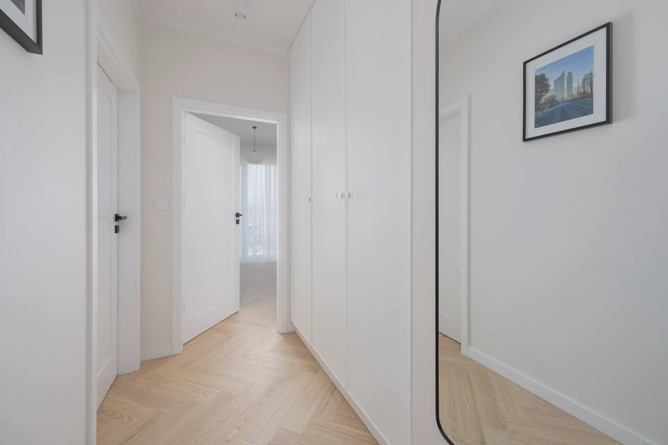 A hallway with light wooden flooring and white walls leading to different rooms. Built-in wardrobes add storage while maintaining a clean look.