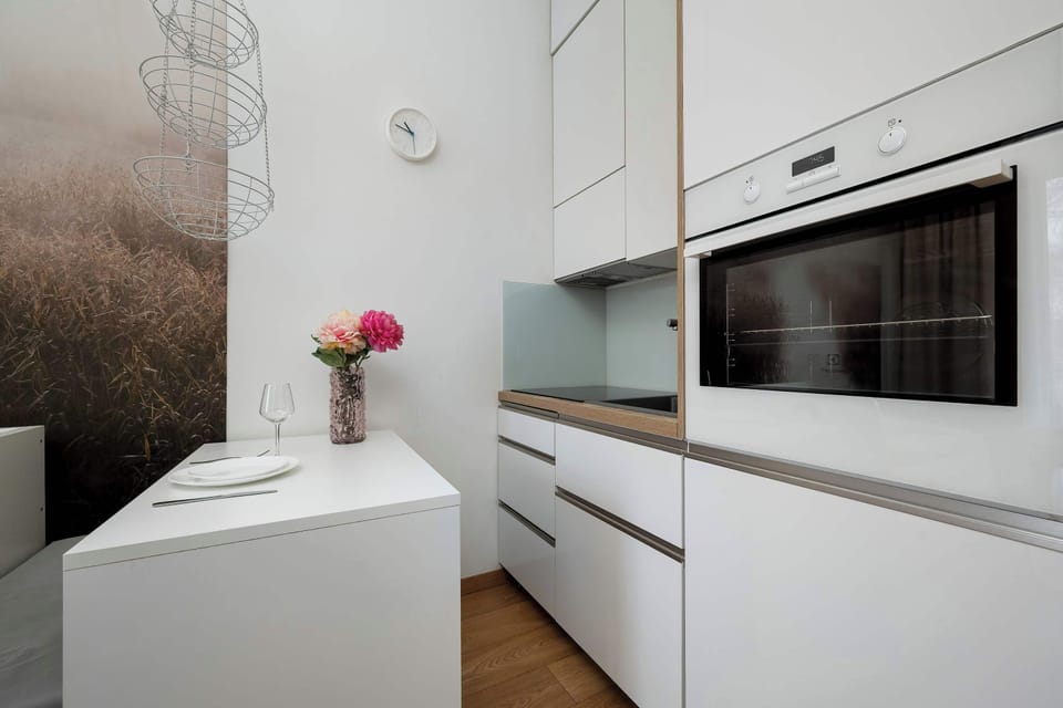 A compact kitchenette view shows the integrated oven and streamlined white handleless cabinets. A small white dining table with two chairs is conveniently placed next to the cooking area.