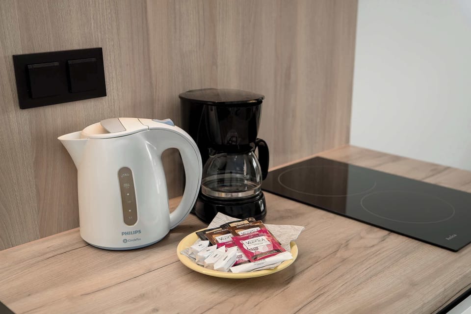 A kitchenette counter with a kettle, coffee maker, and cups. Everything is neatly arranged for convenience.