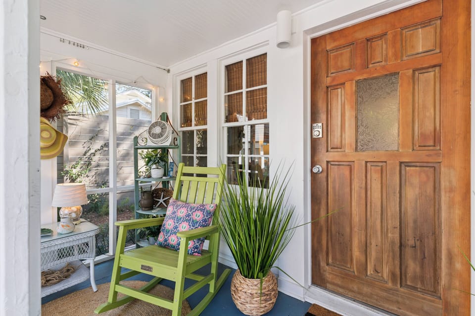 Your charming front porch welcomes you with a cozy green rocking chair and tropical touches, perfect for morning coffee.
