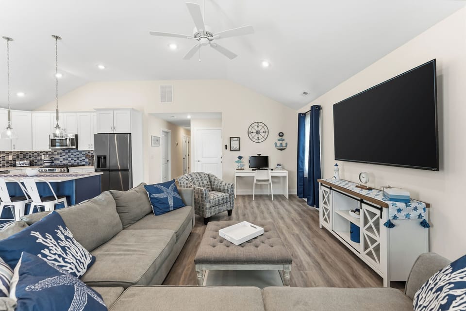 Bright coastal living room with large sectional, big TV, and open kitchen