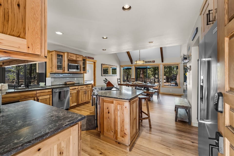 Your spacious kitchen invites culinary adventures with granite counters, rich wood cabinets, and forest views through every window.