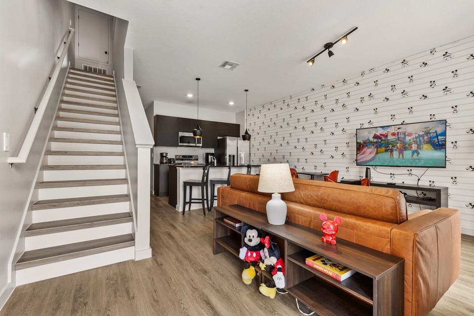Modern living area with a leather sofa, open kitchen, and playful mickey mouse wallpaper.