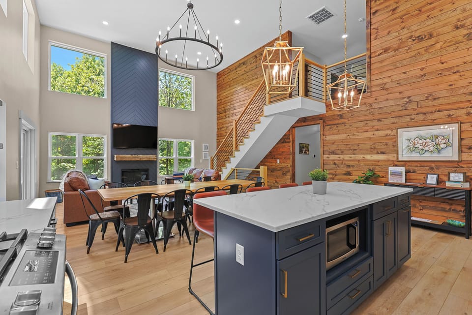 Open-concept kitchen, dining, and living space with an electric fireplace, deck access with grill, and beautiful views of the surrounding woods.