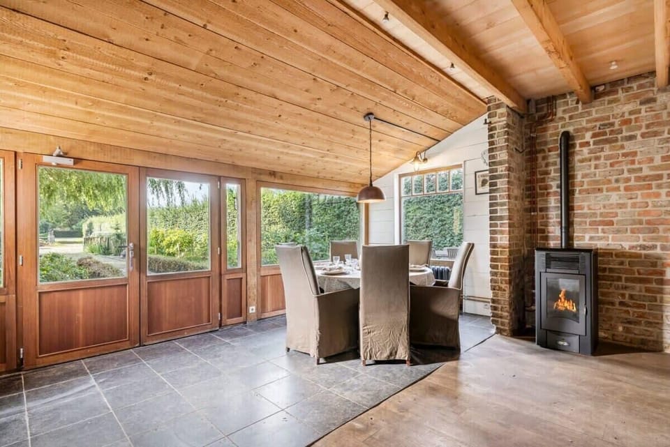 Dining area with large windows, a wood ceiling, and a cozy fireplace.