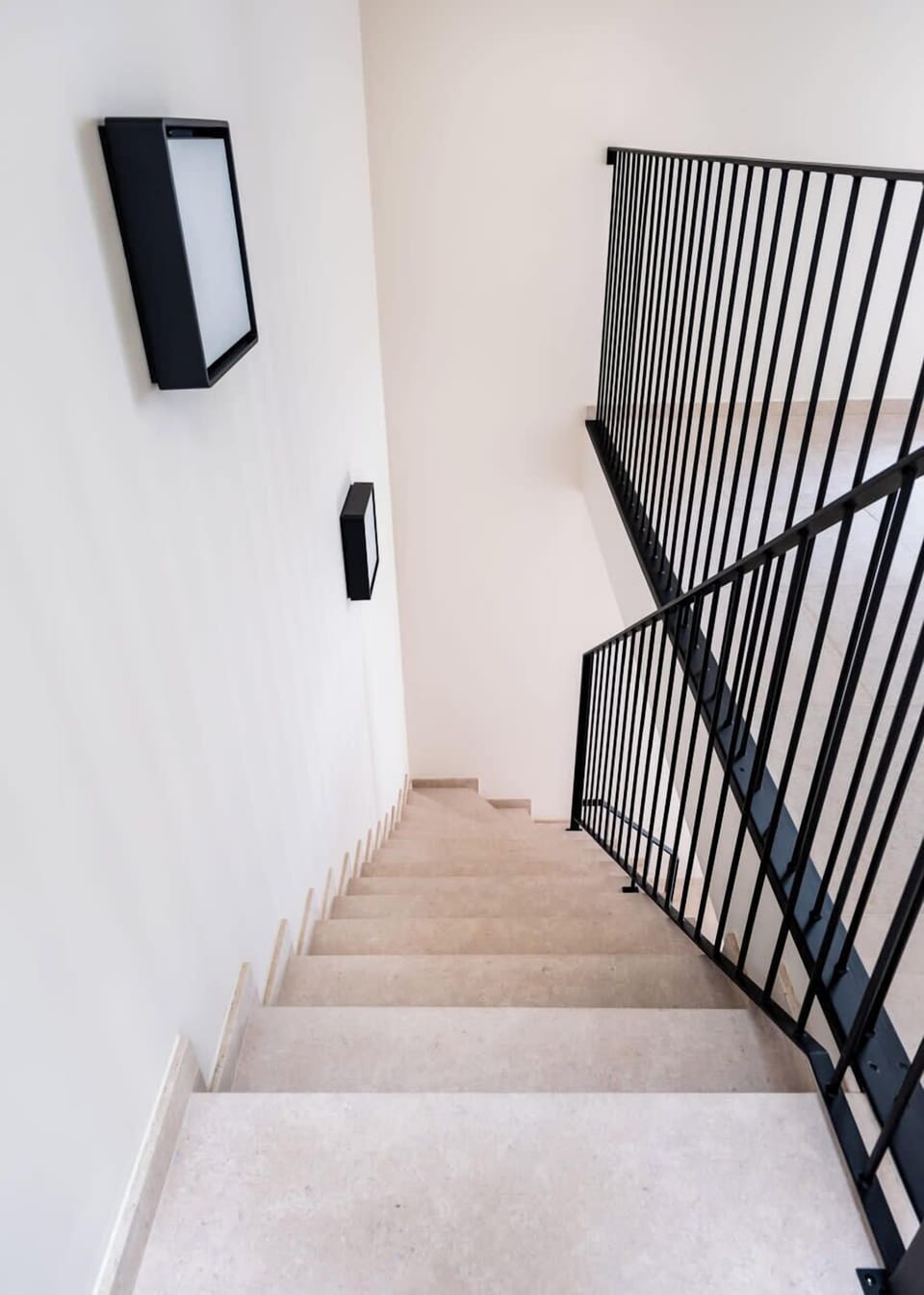 Modern staircase with black metal railing and wall-mounted lights