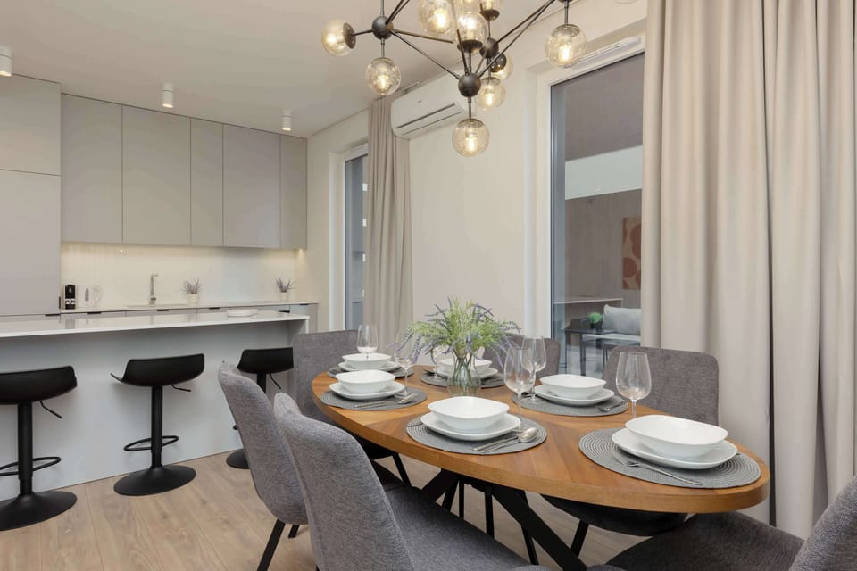 A modern dining space next to a kitchen island with bar stools and table settings prepared.