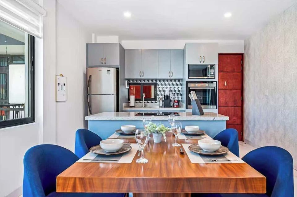 Dining space w/ wood table & blue chairs beside modern kitchen