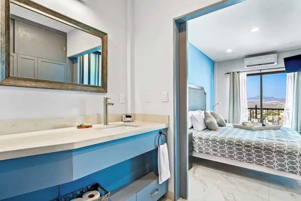 Bright bedroom w/ bed, mirror & open doorway to bathroom