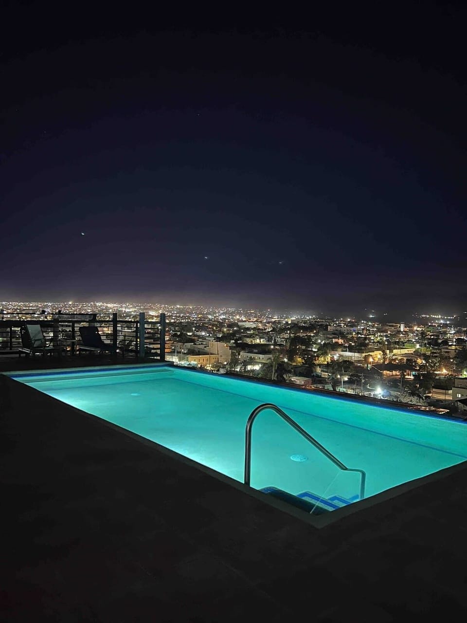 Rooftop pool glowing at night w/ city lights stretching into the distance