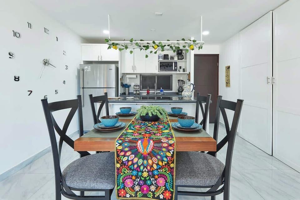 Dining table set for meals w/ colorful runner and open flow into the kitchen