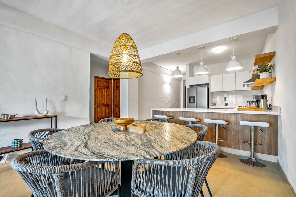 Marble-top dining table with woven chairs under a woven pendant light fixture.