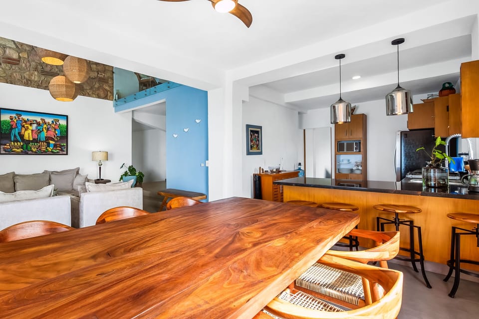 Close-up of a large solid wood dining table looking across to the open-plan living area and the kitchen breakfast bar.