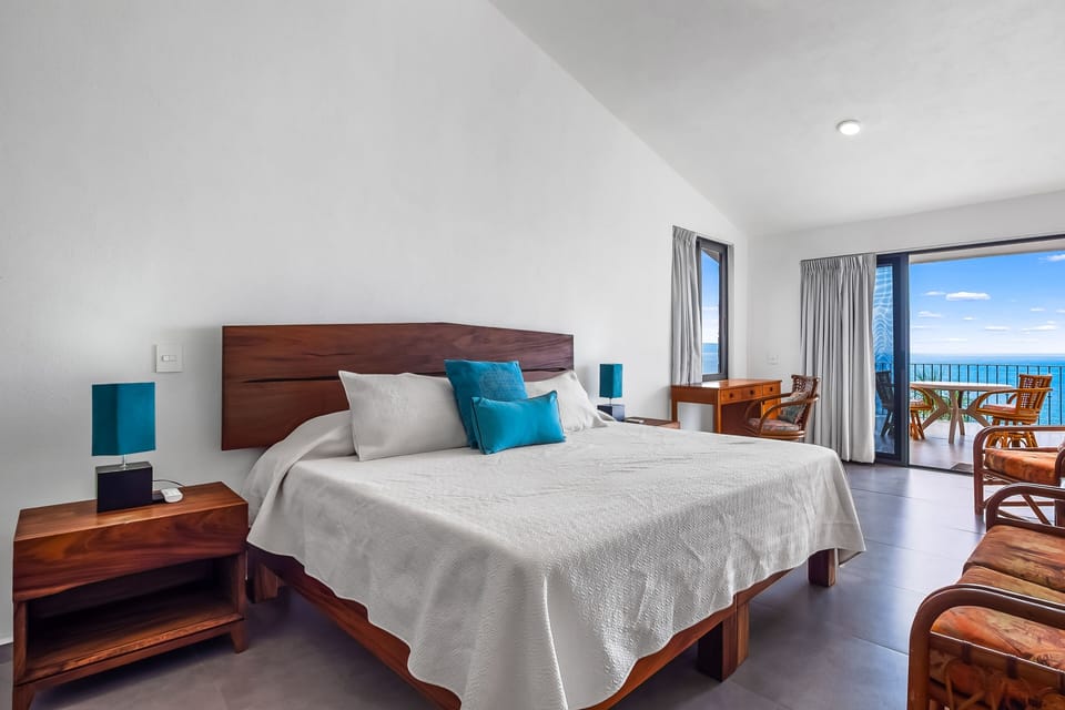 Spacious bedroom featuring a large wooden bed, clean white walls, and sliding glass doors that open to a scenic balcony.