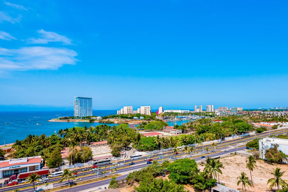 Enjoy a wide, sun-drenched view of the shimmering blue bay, sandy shores, and vibrant city infrastructure stretching into the distance.