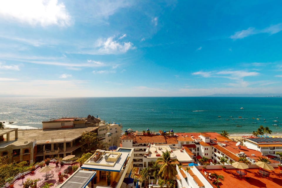 Stunning high-altitude view showcasing the expansive blue ocean, sunny sky, and rooftops of the coastal neighborhood.