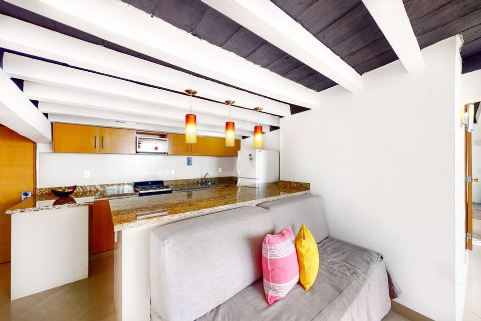Close-up of the integrated kitchen space highlighting a long granite breakfast bar, wooden cabinetry, and modern pendant lighting.