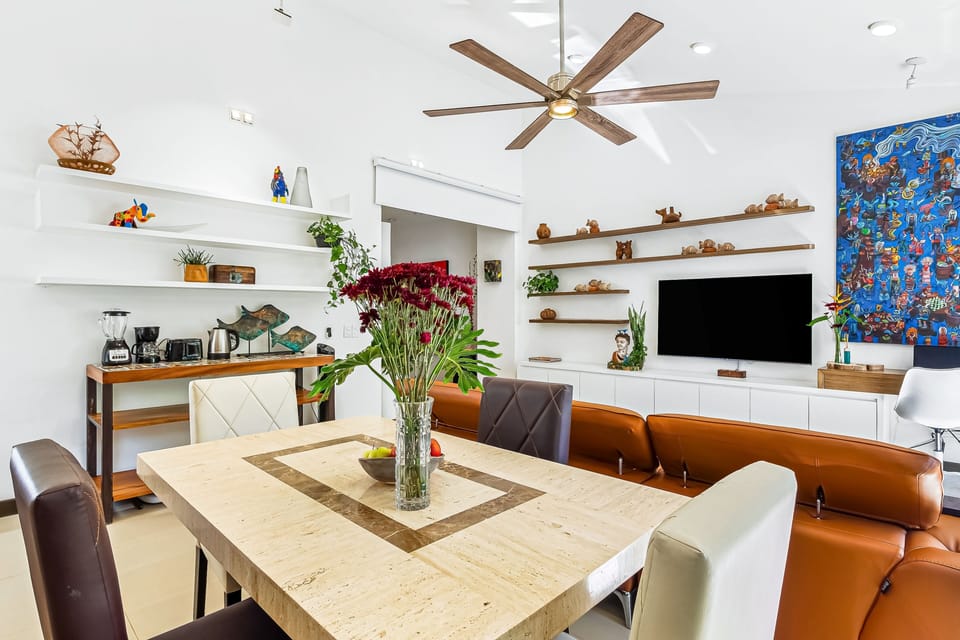 Bright dining layout overlooking the adjacent living area, complete with a ceiling fan and flat-screen TV.