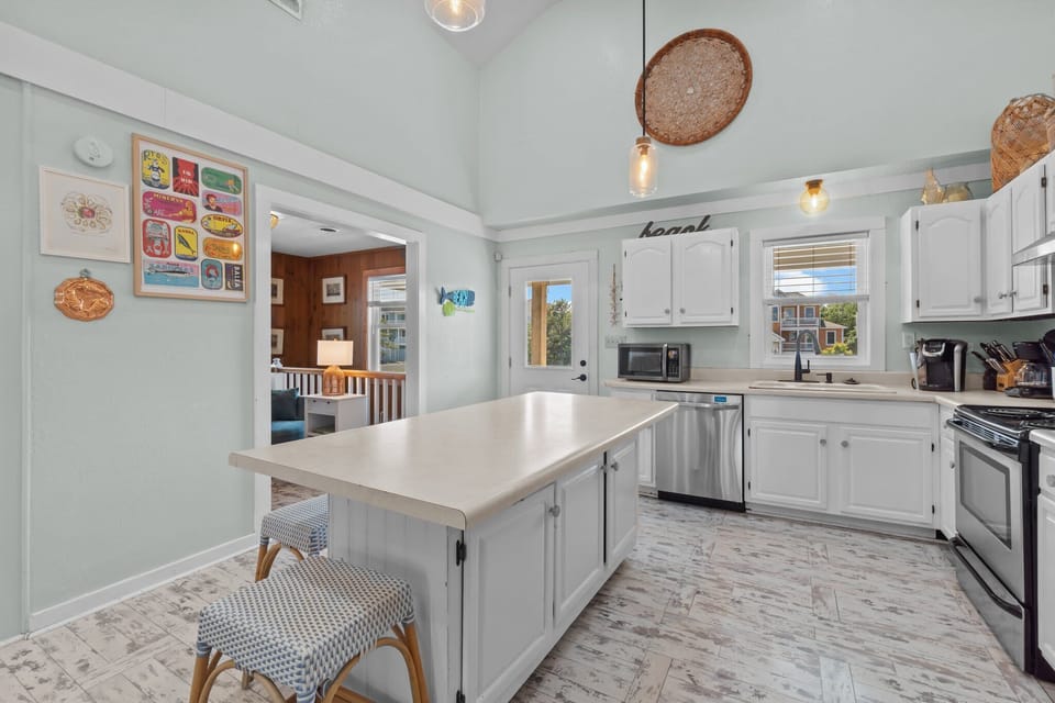 Kitchen w/ Stainless Steel Refrigerator, Electric Range & Oven,  Microwave, Sink, Cooking Utensils, Center Island w/ Bar Seating, and White Cabinetry