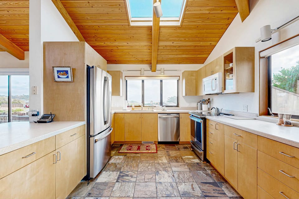 Natural light pours through the skylights and fills the spacious kitchen, where warm wood cabinetry and stone floors complement the coastal setting.