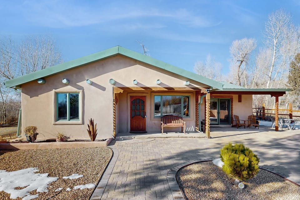 Arrive to a classic adobe framed by green metal roofing and a welcoming covered entry