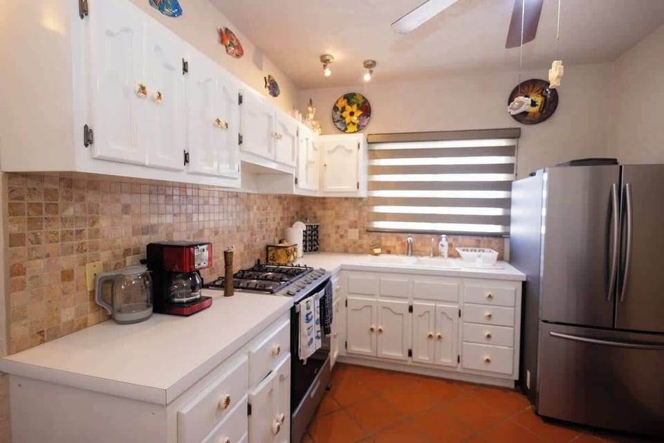 Compact kitchenette w/ white cabinetry, counter space & stainless fridge for simple cooking