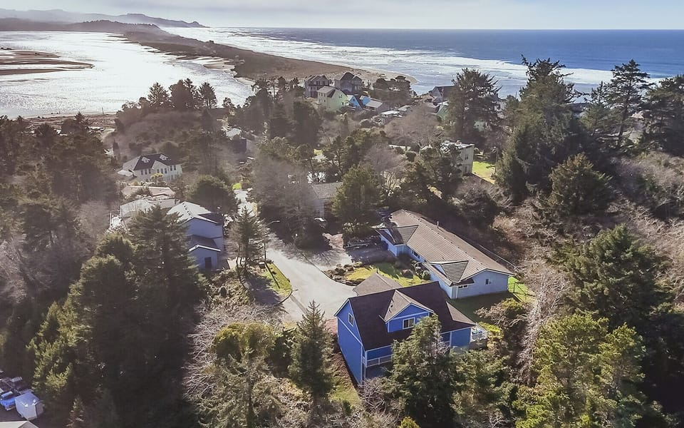 Aerial view of coastal residential community nestled among trees, with pristine beach and ocean waves visible in the distance.