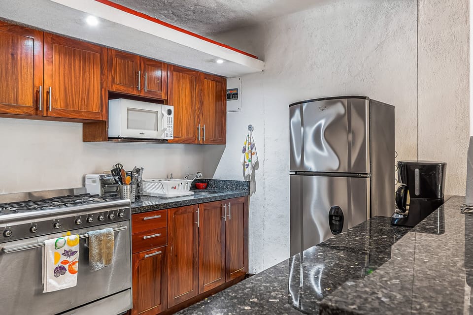 Well-appointed kitchen featuring warm wood cabinetry, dark granite countertops, a built-in microwave, stainless steel gas stove, refrigerator, and coffee maker, providing everything needed for home-cooked meals.