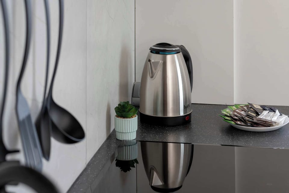 The black kitchen utensils and a silver electric kettle are arranged neatly on a dark, reflective countertop. The shiny surface mirrors the items, emphasizing a tidy and sophisticated kitchen environment.