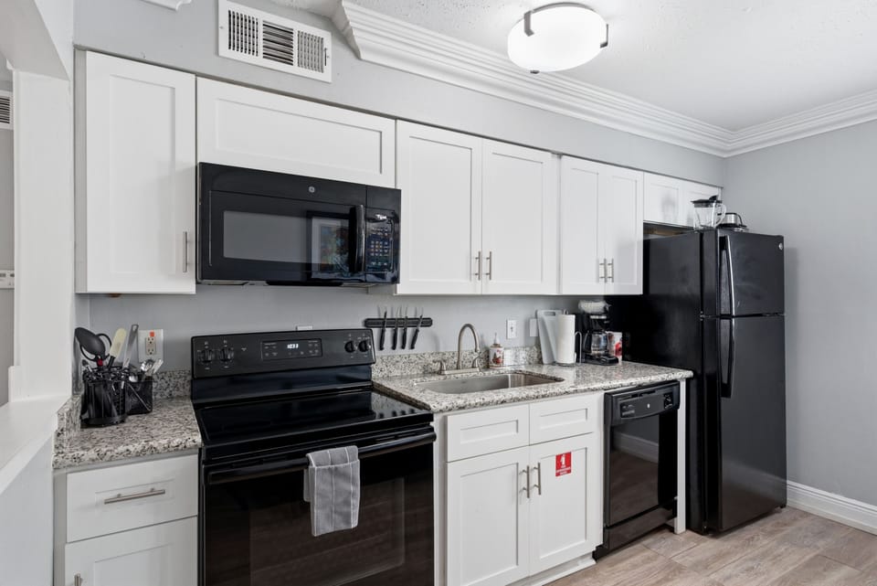 Unit 203 modern kitchen w/ crisp white cabinetry & black appliances.
