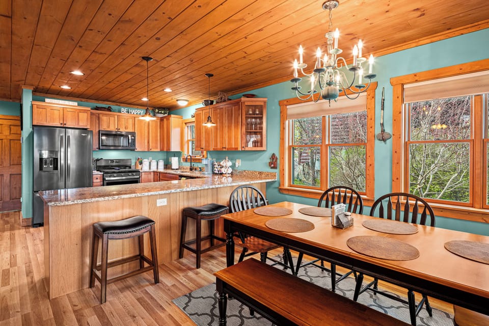 Warm cabin kitchen with wood cabinets, island, dining table, windows, trees view