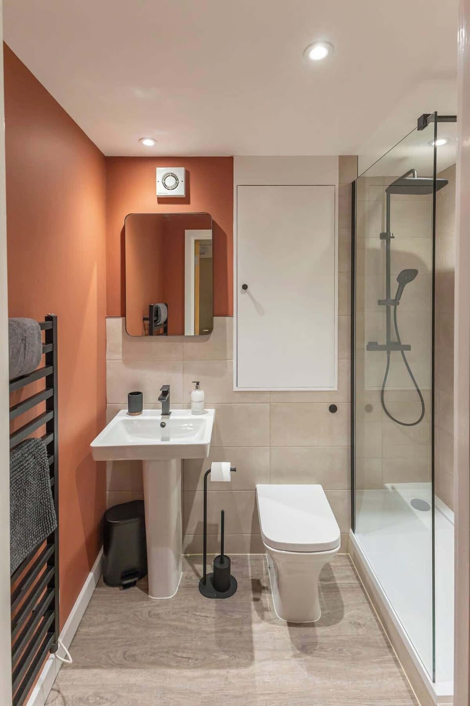 Bathroom with a walk-in glass shower and clean tiled finishes. Bright vanity space with contemporary fixtures and a warm accent wall adds a stylish touch.