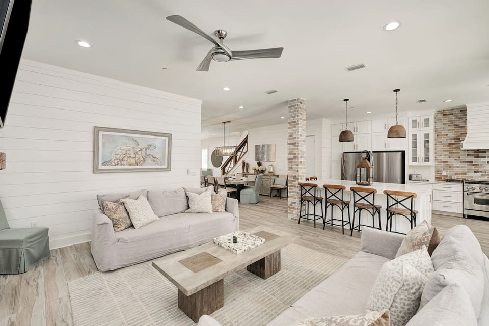 Step into your coastal retreat with soaring ceilings, shiplap walls, and inviting open-concept design connecting plush seating, dining, and a chef's kitchen for effortless gathering and relaxation.