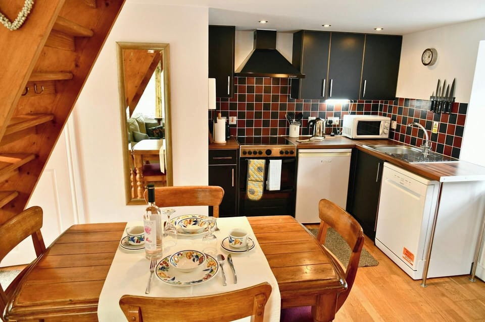 Wooden dining table set for four beside a kitchen with dark cabinets and tiled splashback