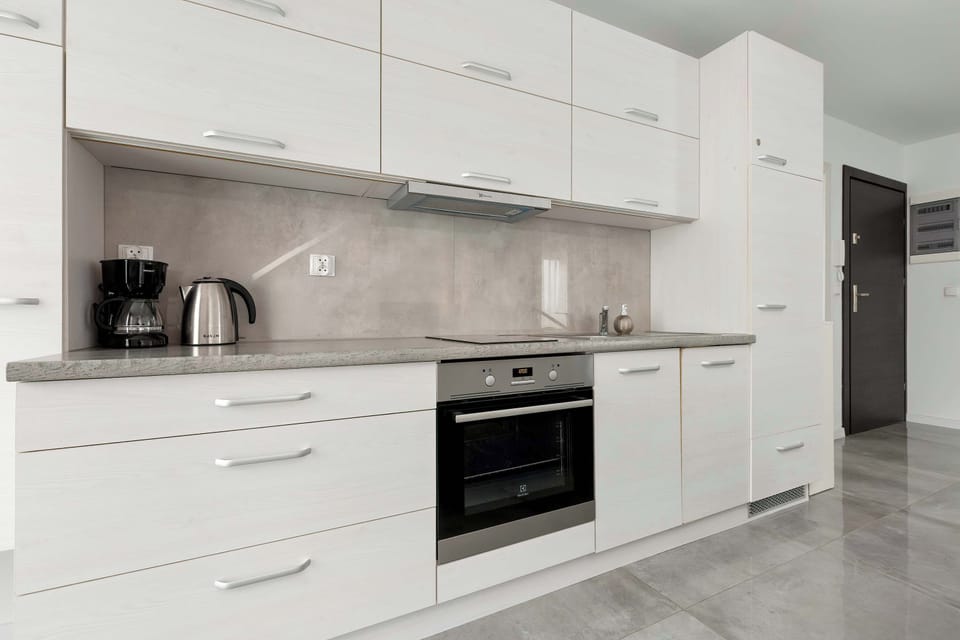 The sleek, white kitchenette is equipped with modern appliances, including a built-in oven, a kettle, and a coffee maker on the countertop.