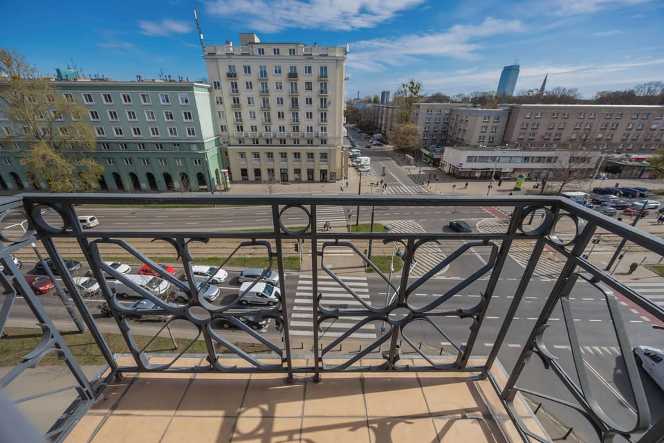 A balcony with a decorative metal railing overlooking the city. The space offers a pleasant spot to enjoy fresh air and take in the surrounding views.
