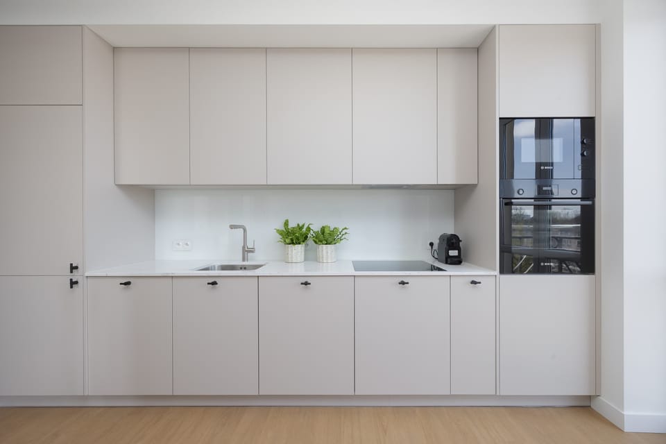 A fully fitted kitchenette with light cabinetry and integrated appliances. Clean lines and a neutral color palette give the space a contemporary and elegant feel.