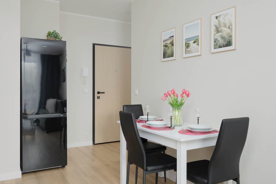 A dining area with a small table set for a meal, including plates and glasses. A refrigerator stands nearby, blending into the open-plan space. The setting feels tidy and ready for use.