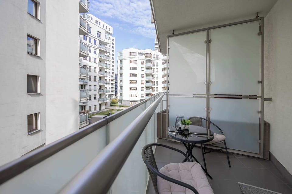 A narrow balcony with a small table and chairs overlooking nearby buildings.