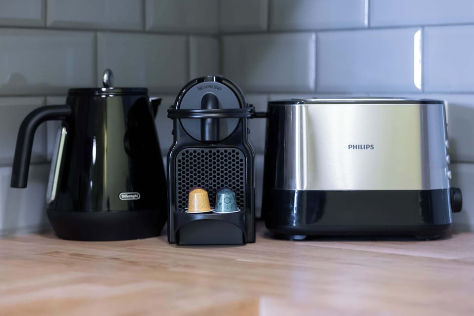 A stylized still life featuring an electric kettle and a modern, compact coffee maker (like a Nespresso) resting on a kitchen counter surface.