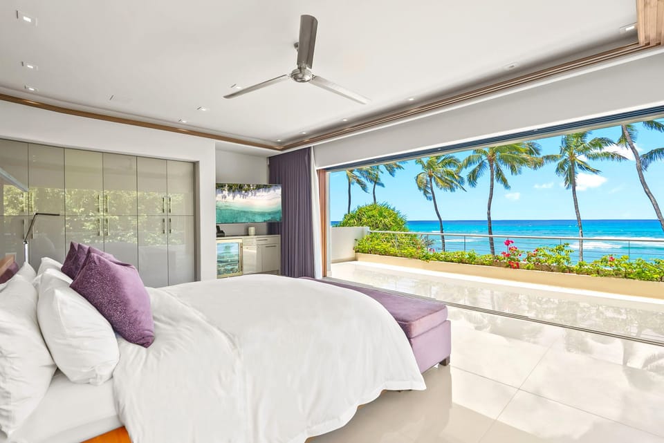 Wake up to paradise in this elegant bedroom, where floor-to-ceiling glass doors frame stunning ocean views and swaying palms. Your private retreat features a plush king bed and direct access to a sun-drenched terrace overlooking turquoise waters.