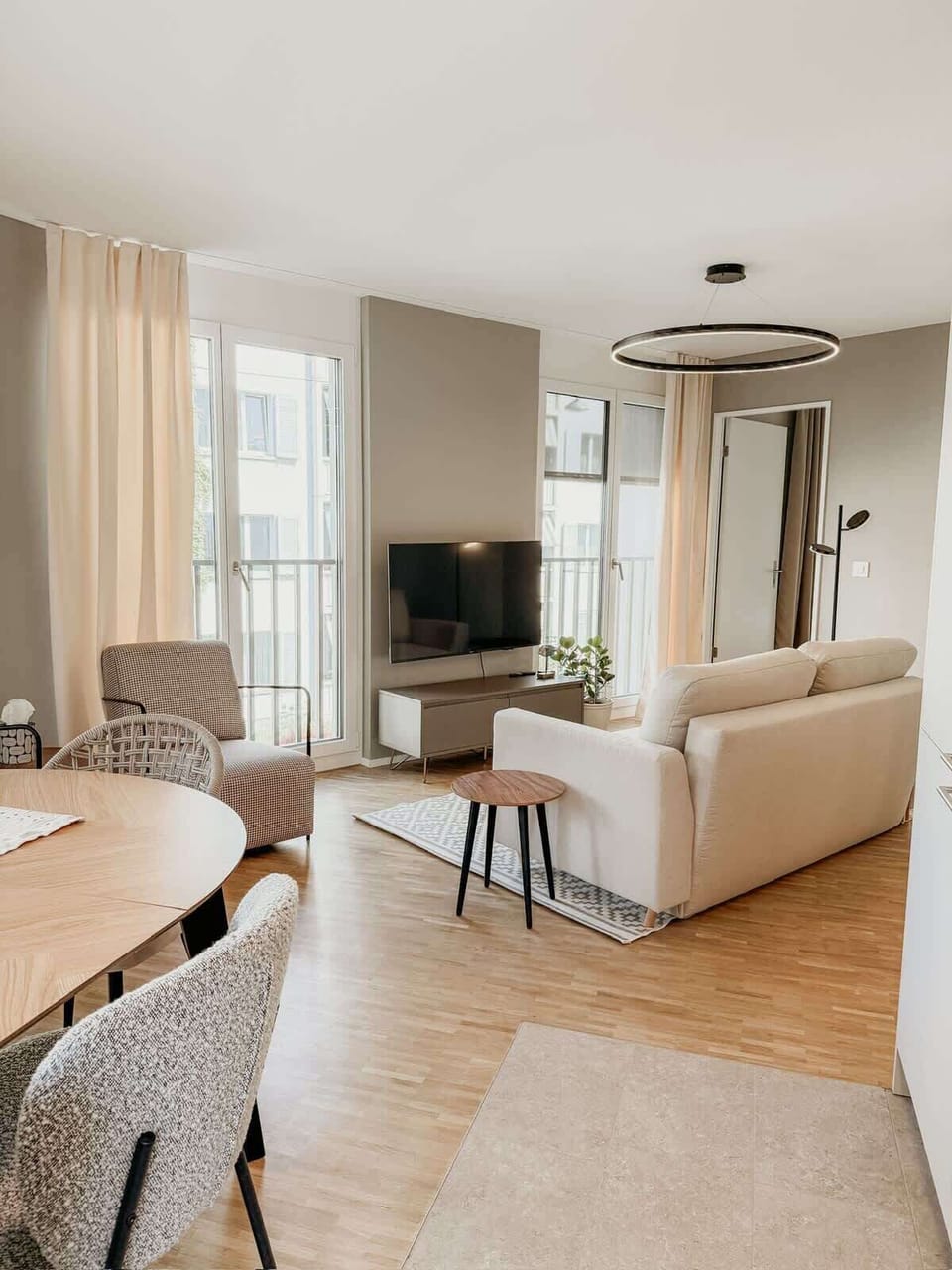 Gemütlicher Wohnbereich mit Smart-TV, bodentiefen Fenstern und viel Tageslicht. Hochwertiges Sofa, stilvolle Sessel und ein eleganter Essbereich schaffen eine entspannte Atmosphäre – ideal zum Wohlfühlen und Abschalten.