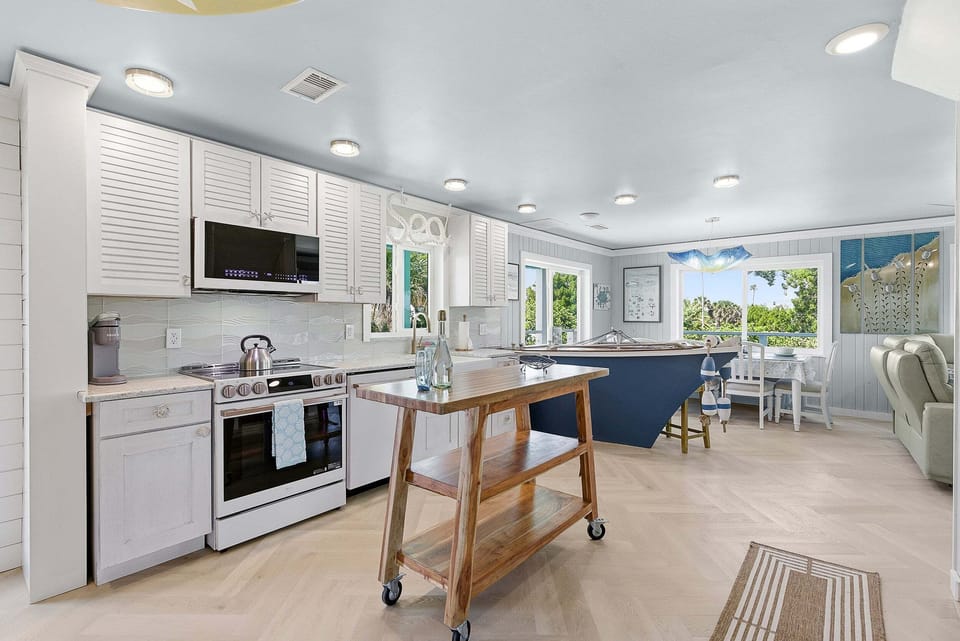 Stylish coastal kitchen featuring modern appliances, island workspace, and sunlit dining area. Perfect for your beach stay, this open layout offers comfort, natural light, and a relaxing space to gather after a day by the shore.