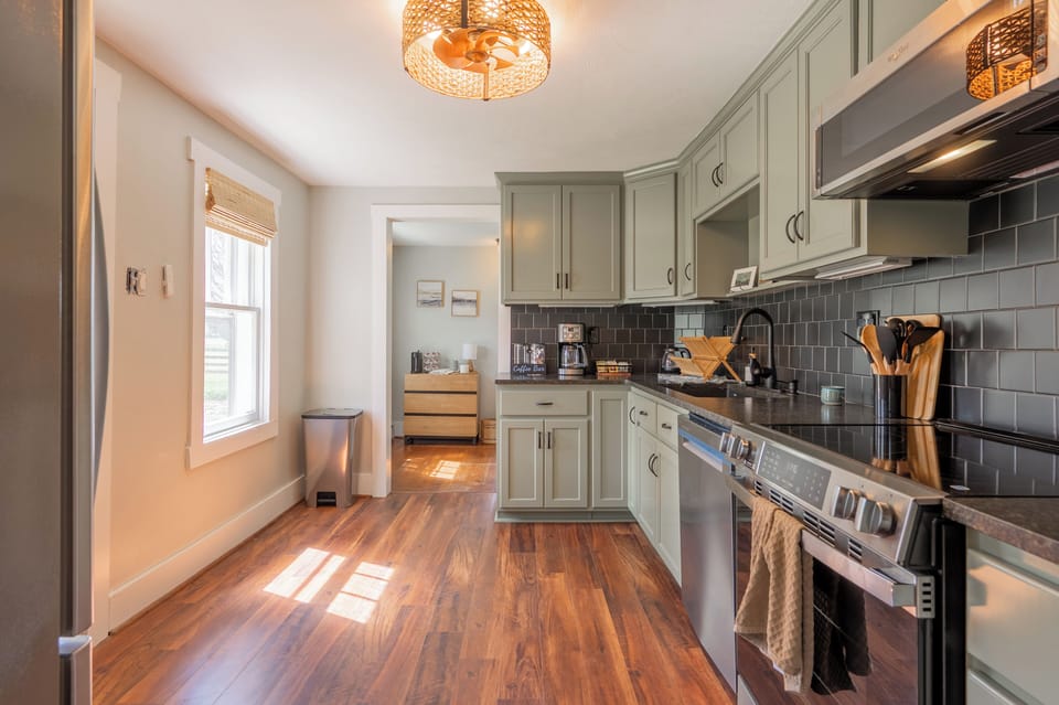 A stylish, modern kitchen featuring sage green cabinets, dark tile backsplash, and warm wood flooring.