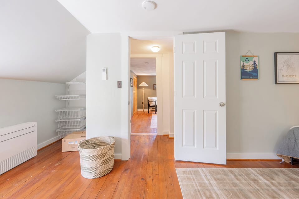 A bright room featuring warm wood floors, a basket, open storage shelving, and a doorway leading into an adjacent space.