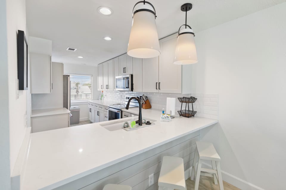 Step into a modern kitchen bathed in natural light, where sleek white cabinetry meets pristine quartz countertops. The centerpiece island invites you to gather, cook, and create memories with ease.