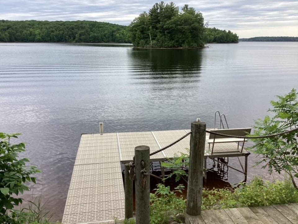 Tranquil lake with private dock extending into calm waters, surrounded by lush forested shoreline and peaceful natural beauty.